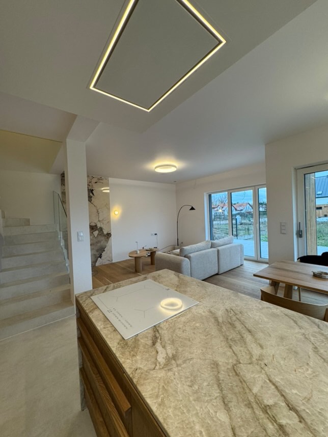 Nowoczesne wnętrze domu z marmurową wyspą kuchenną, podświetlanym sufitem i drewnianą podłogą.