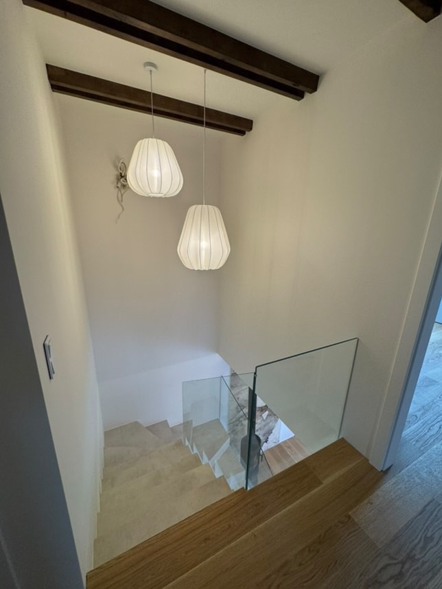 Klatka schodowa z drewnianymi stopniami, szklanymi balustradami i dwoma wiszącymi lampami w kształcie kokonów, widok z góry.