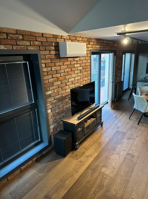 Wykończony salon w Piasecznie z ceglaną ścianą, klimatyzacją, telewizorem na szafce w stylu industrialnym i drewnianą podłogą.