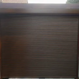 Zewnętrzna, brązowa roleta zamknięta, widoczna na tle ściany z poziomych paneli w podobnym odcieniu brązu, z elementami srebrnego wykończenia po bokach.
