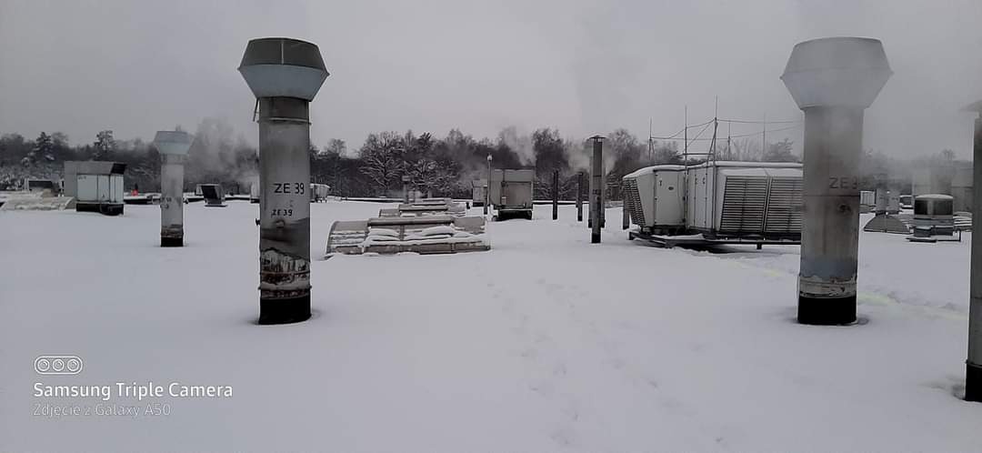 Zaśnieżony dach z kominami wentylacyjnymi i urządzeniami klimatyzacyjnymi, widok z góry w pochmurny dzień.