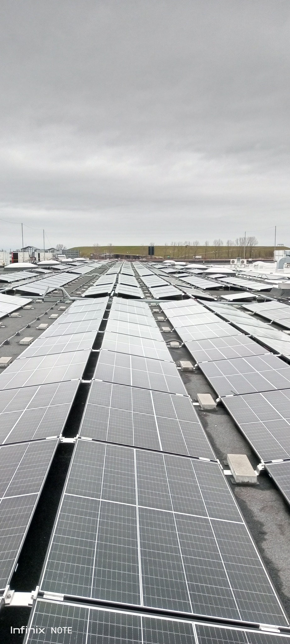 Rozległa instalacja paneli słonecznych na dachu budynku przemysłowego, widok z góry przy pochmurnej pogodzie.