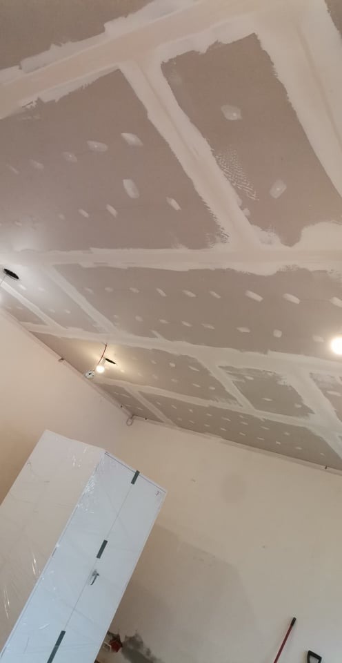 Sufit z płyt gipsowo-kartonowych w trakcie szpachlowania, widoczne łączenia i wkręty, z boku częściowo owinięta folią biała szafa.