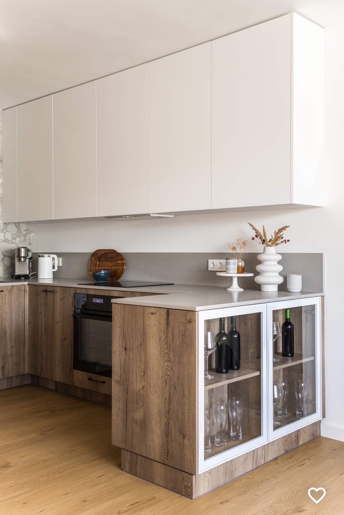 Nowoczesna kuchnia z drewnianymi szafkami dolnymi i białymi górnymi, szklana witryna z winami i kieliszkami, minimalistyczny wystrój.