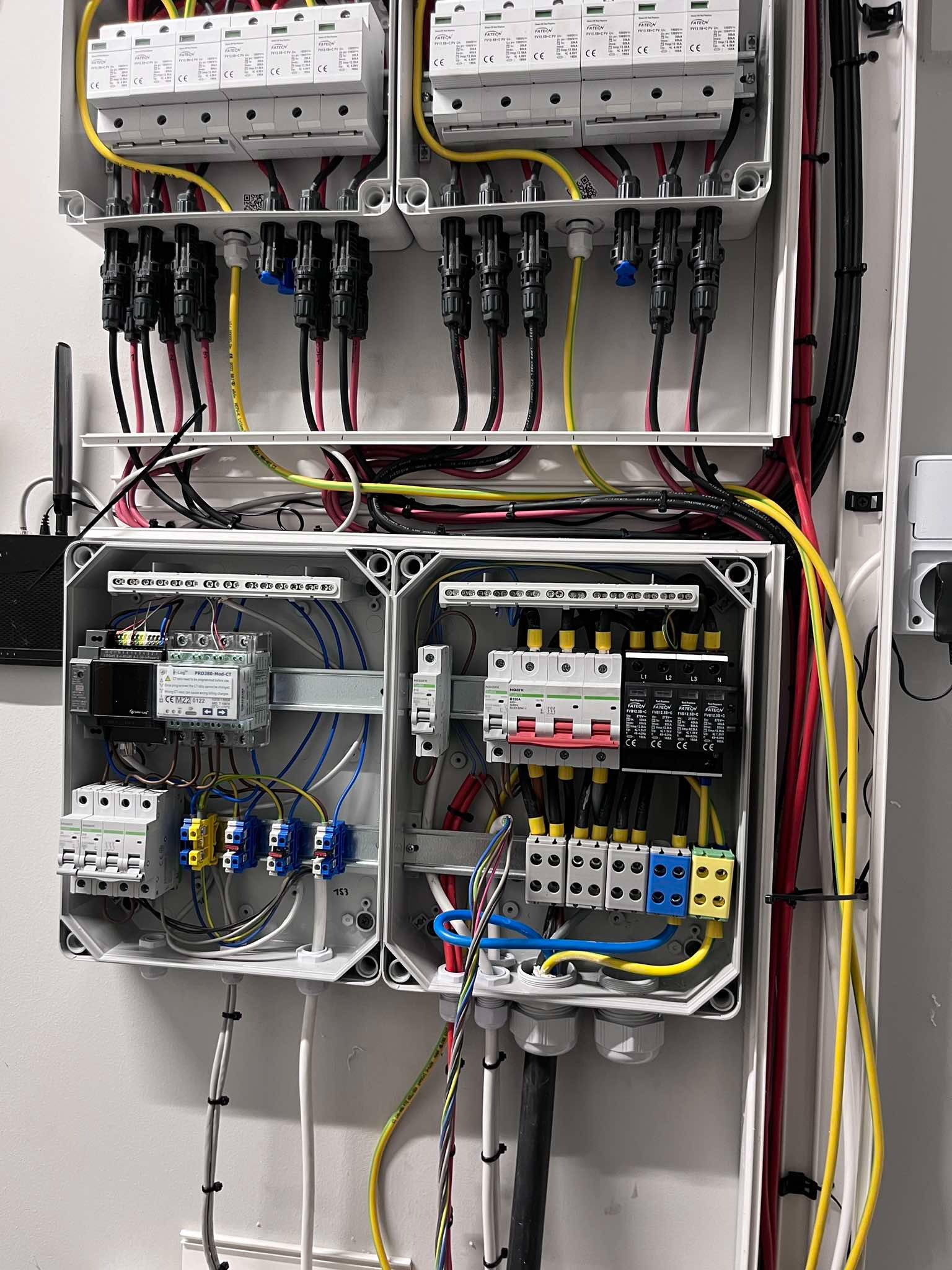 Rozdzielnia elektryczna z zabezpieczeniami przepięciowymi i różnicowoprądowymi w białej obudowie, widoczne kable i przewody w różnych kolorach.