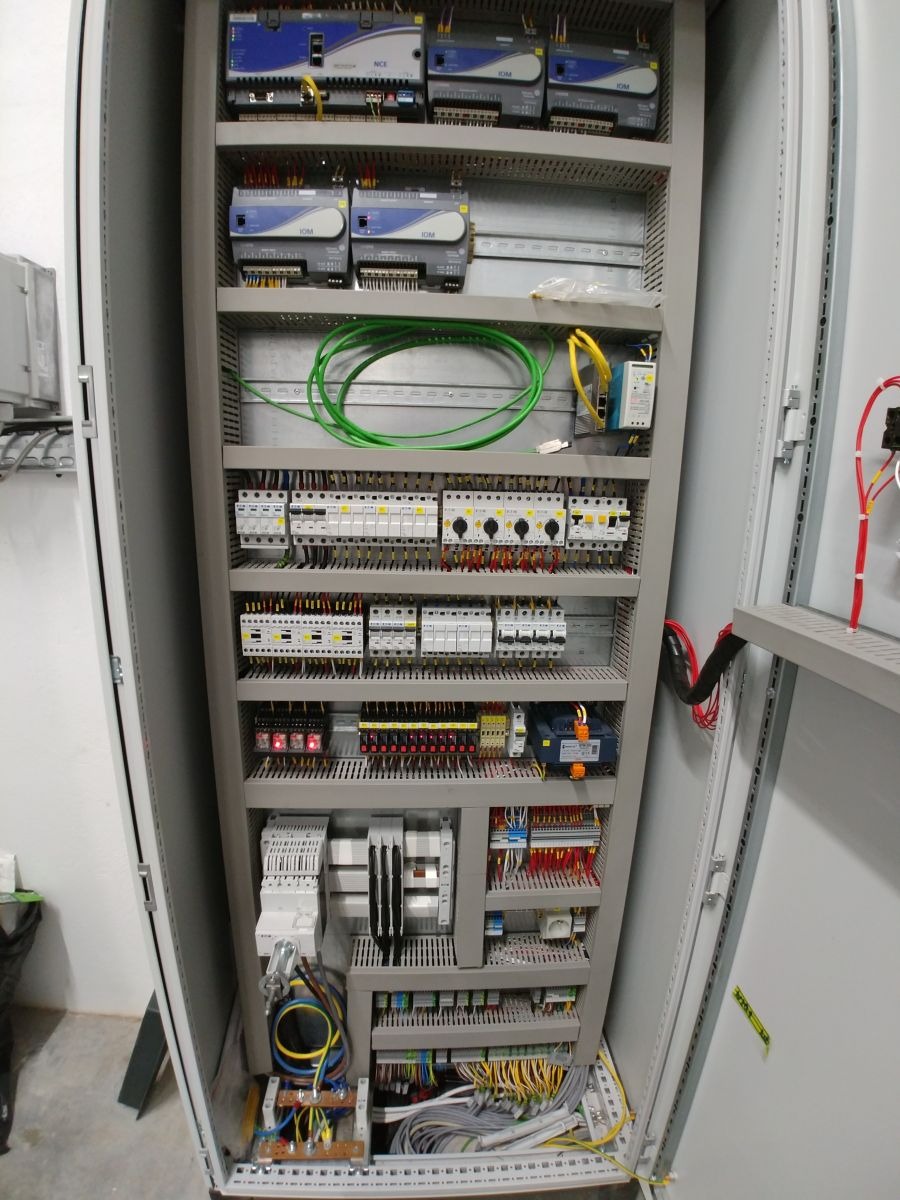 Otwarta szafa sterownicza z widocznymi modułami, przewodami i zabezpieczeniami. Zastosowano przewody w różnych kolorach. Widoczne elementy automatyki przemysłowej.