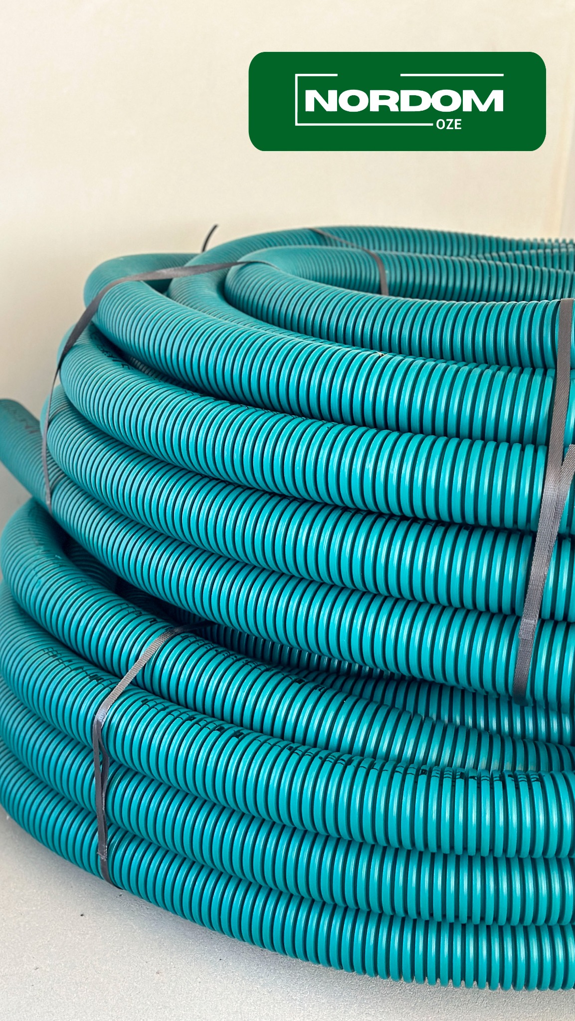 Zwój elastycznej, karbowanej rury wentylacyjnej w kolorze turkusowym, spięty szarą taśmą, widoczne logo producenta NORDOM OZE w lewym górnym rogu.