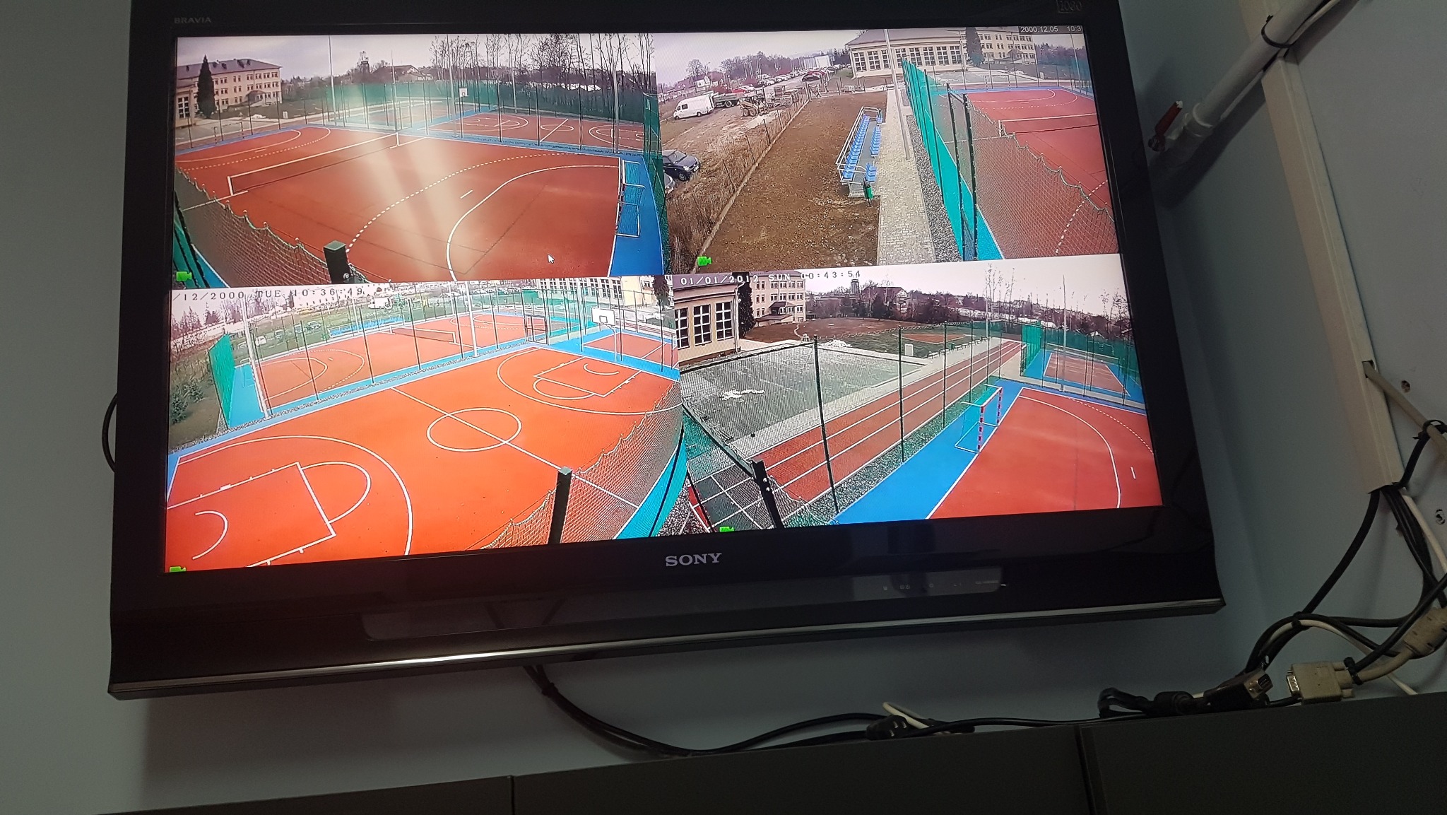 Ekran monitoringu z podglądem boisk sportowych z różnych kamer. Widoczne korty tenisowe i boiska do koszykówki z perspektywy kamer przemysłowych.