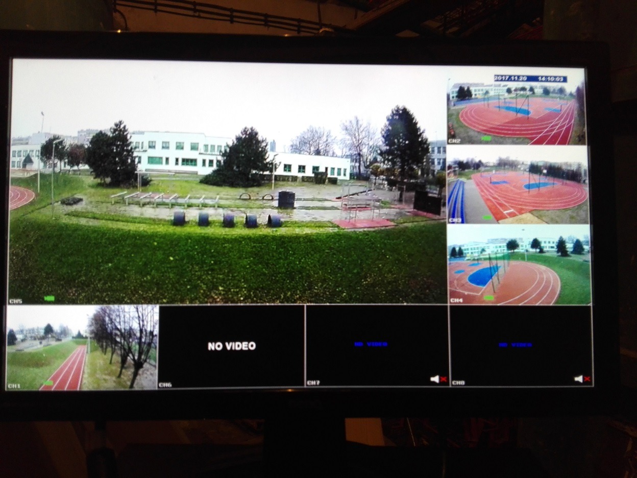 Ekran monitoringu z widokiem na boisko sportowe i budynek szkolny z kilku kamer. Dolne okna pokazują brak sygnału. Data i godzina w prawym górnym rogu.