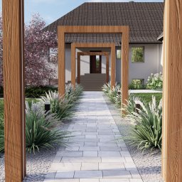 GreenEM Michał Flekiej - Nowoczesny ogród z kamienną ścieżką, ozdobnymi trawami i drewnianą pergolą prowadzącą do domu. Kwitnące drzewo wiśniowe dodaje koloru.