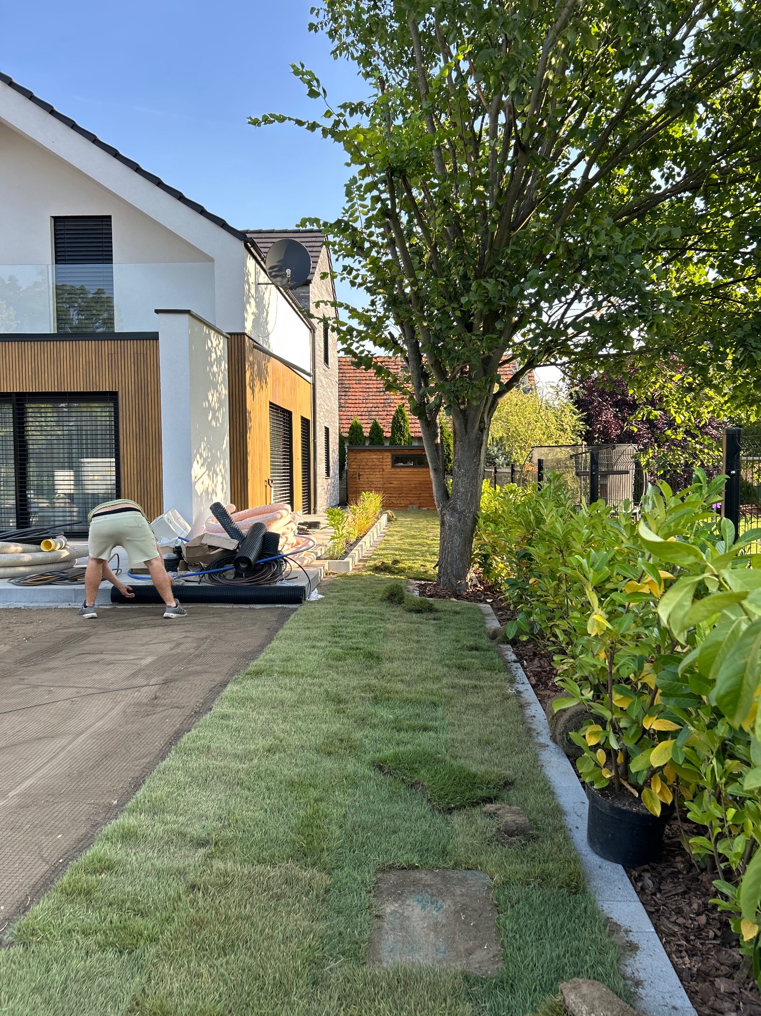 Układanie trawy z rolki w Mąkoszycach. Widoczny fragment ułożonego trawnika, przygotowane podłoże i rolki trawy. Prace ogrodnicze przy nowoczesnym domu.