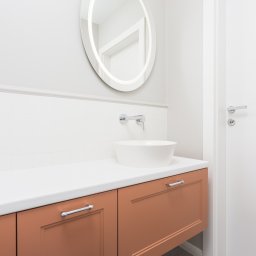 KATARZYNA BENKO OCH-ACH_CONCEPT - Nowoczesna łazienka z okrągłym lustrem podświetlanym LED, minimalistyczną umywalką nablatową i brązowymi szafkami pod umywalką z chromowanymi uchwytami.