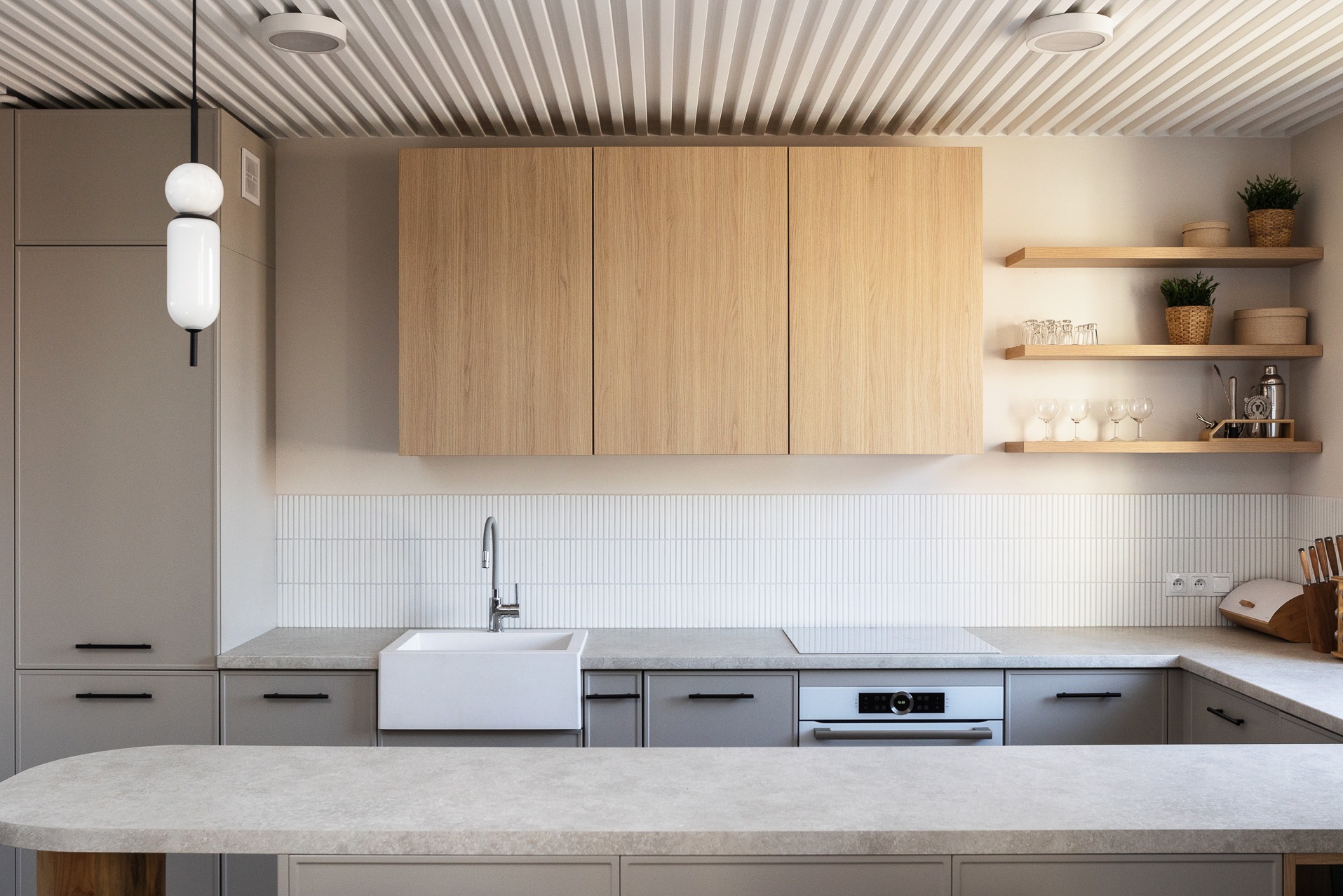 Nowoczesna kuchnia z szarymi szafkami, drewnianymi frontami górnych szafek i białym zlewem farmerskim, oświetlona wiszącą lampą z kulistymi elementami.