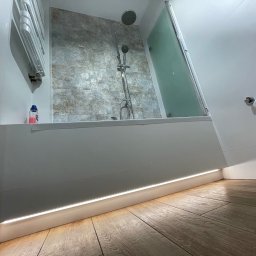 Przedsiębiorstwo Inwestycyjne KBK Dawid Kubik - Nowoczesna łazienka po remoncie: kabina prysznicowa, płytki imitujące kamień, podświetlenie LED przy podłodze i drewnopodobne płytki podłogowe.