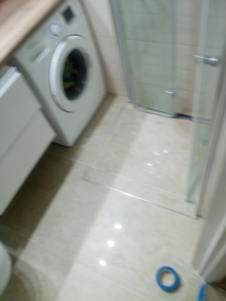 Ukończona łazienka z pralką, kabiną prysznicową i jasnymi płytkami podłogowymi, widoczne ślady po taśmie malarskiej na podłodze.