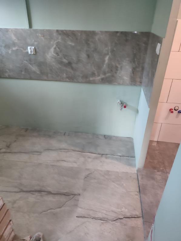 Fragment łazienki w trakcie remontu: szare płytki imitujące marmur na podłodze i ścianie, widoczne przyłącza wodne, zielone ściany, częściowo wykończona ściana z białych płytek.