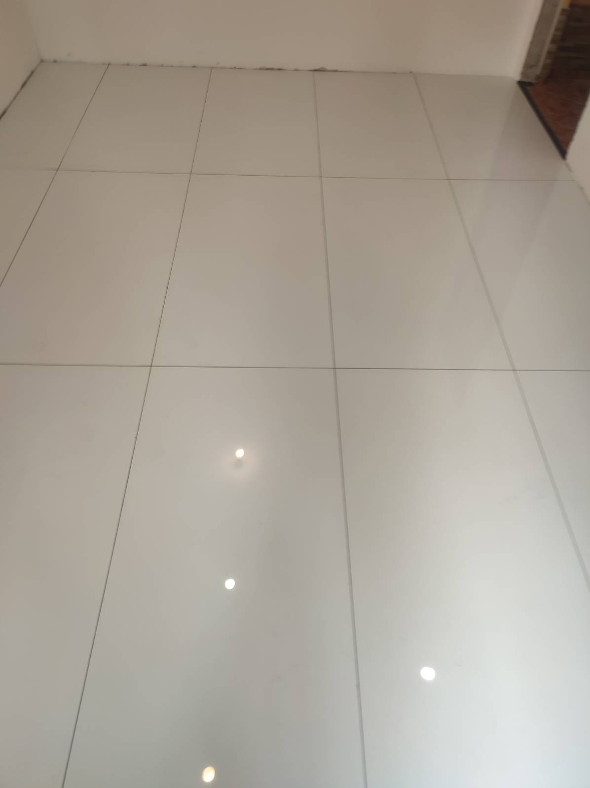 Błyszczące, białe płytki podłogowe z ciemnoszarą fugą, ułożone równo w pomieszczeniu, widoczne odbicia światła na powierzchni płytek.