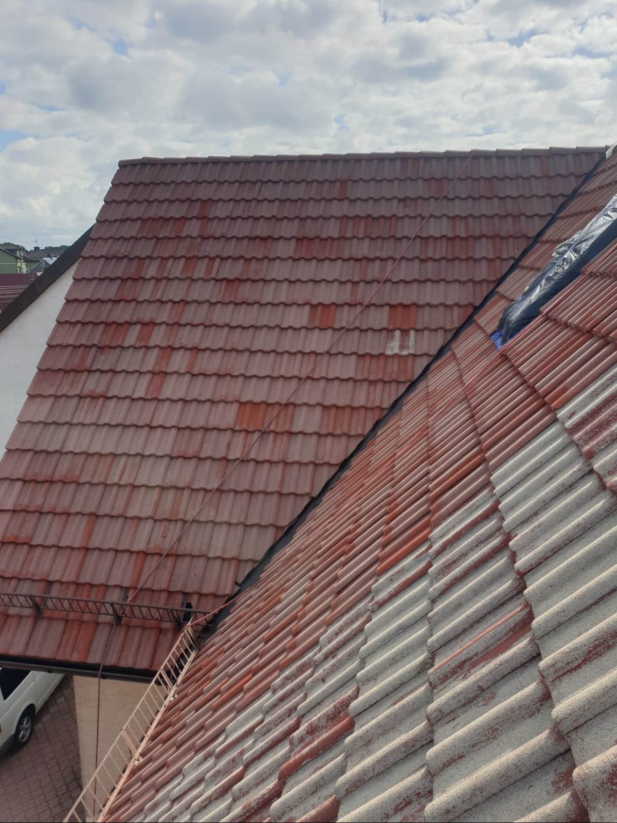 Częściowo umyty dach z czerwonej dachówki, widoczna różnica w kolorze między czystą a brudną powierzchnią, na dachu leży lina zabezpieczająca.