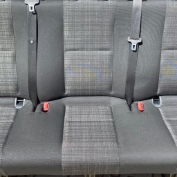 Mateusz Goś - Tapicerka samochodowa z plamą na środkowym siedzeniu, widoczne pasy bezpieczeństwa i mocowania. Tekstylna faktura materiału.