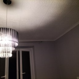 Sabinex - Zamontowany żyrandol z czarnymi abażurami i kryształkami, widoczny na tle białego okna i teksturowanego sufitu w szarym pokoju.