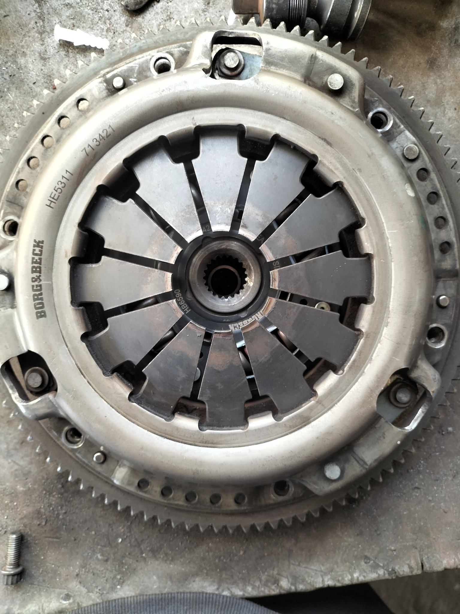 Sprzęgło samochodowe Borg & Beck z widocznymi numerami seryjnymi i zębatym obwodem, leżące na brudnej powierzchni roboczej.