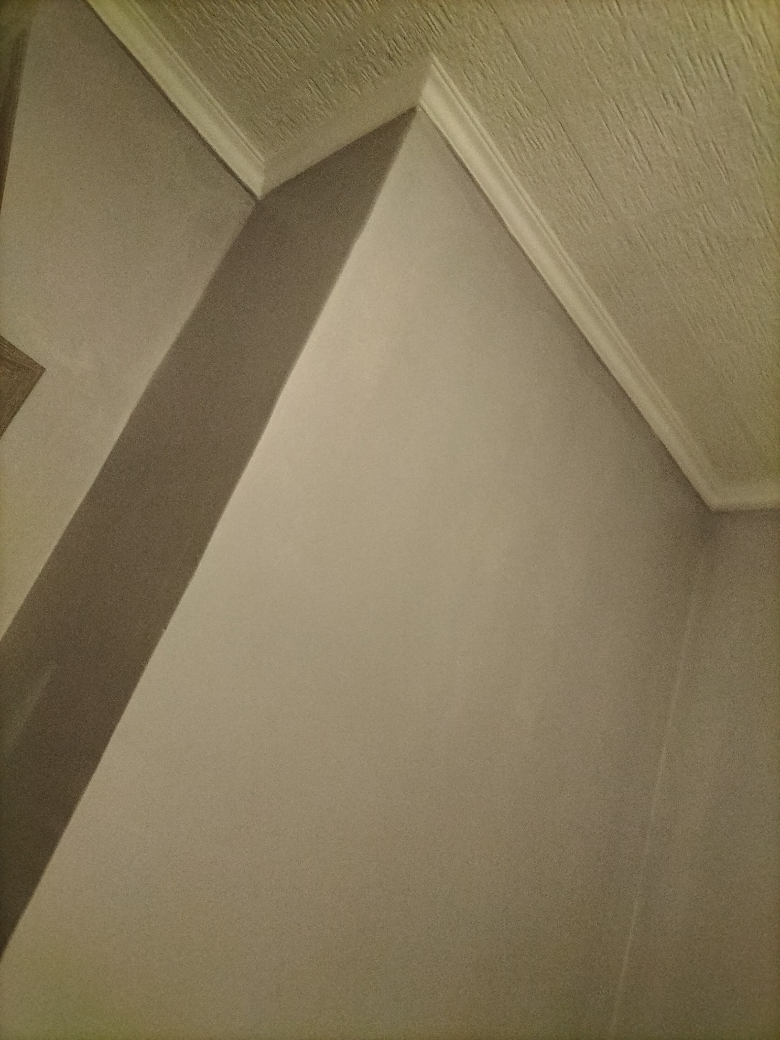 Fragment rogu pokoju z pomalowanymi ścianami w odcieniach beżu, widoczny styk ściany z sufitem i listwa dekoracyjna, sufit z wyraźną fakturą.