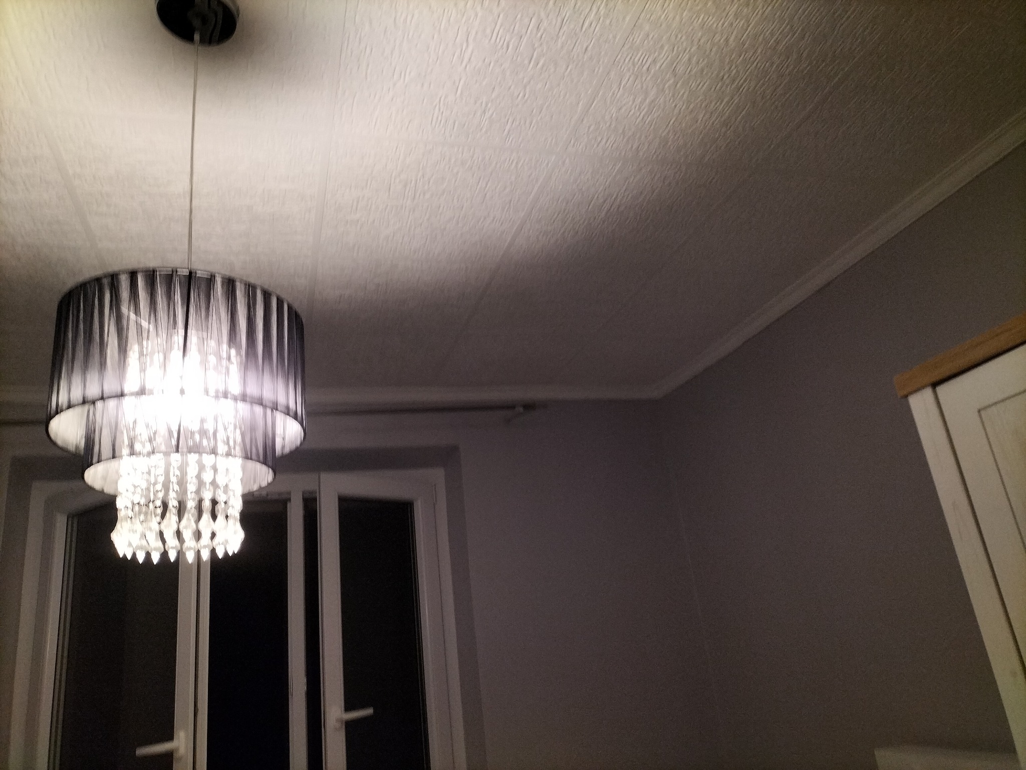 Zamontowany żyrandol z czarnymi abażurami i kryształkami, widoczny na tle białego okna i teksturowanego sufitu w szarym pokoju.