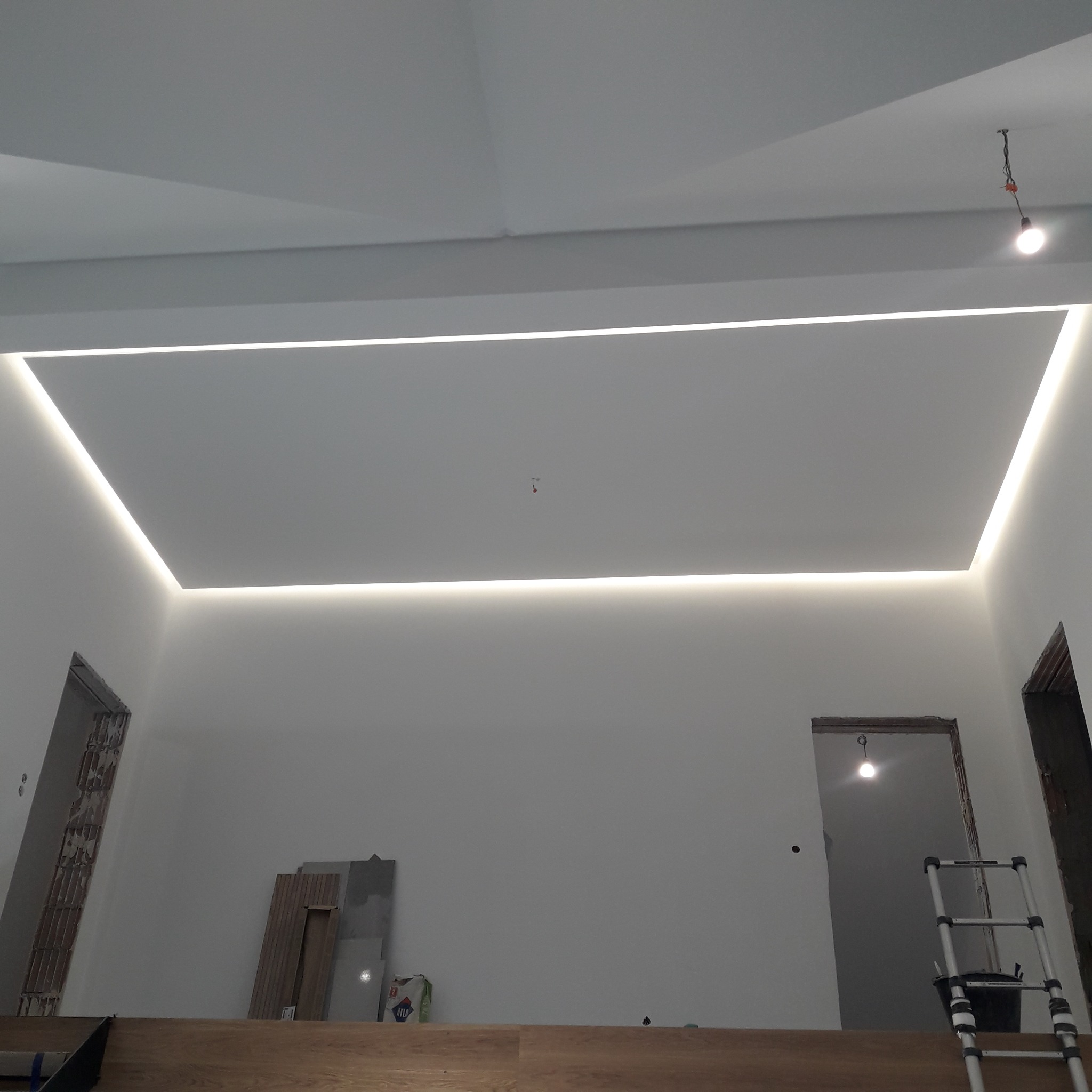 Nowoczesne oświetlenie sufitowe LED w kształcie prostokąta, zrealizowane w Grybowie, widoczne w surowym wnętrzu z elementami w trakcie prac wykończeniowych.