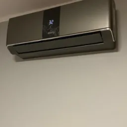 Szary klimatyzator ANDE z wyświetlaczem temperatury 32 zamontowany na ścianie. Nowoczesny design, widok z przodu, oświetlenie naturalne.