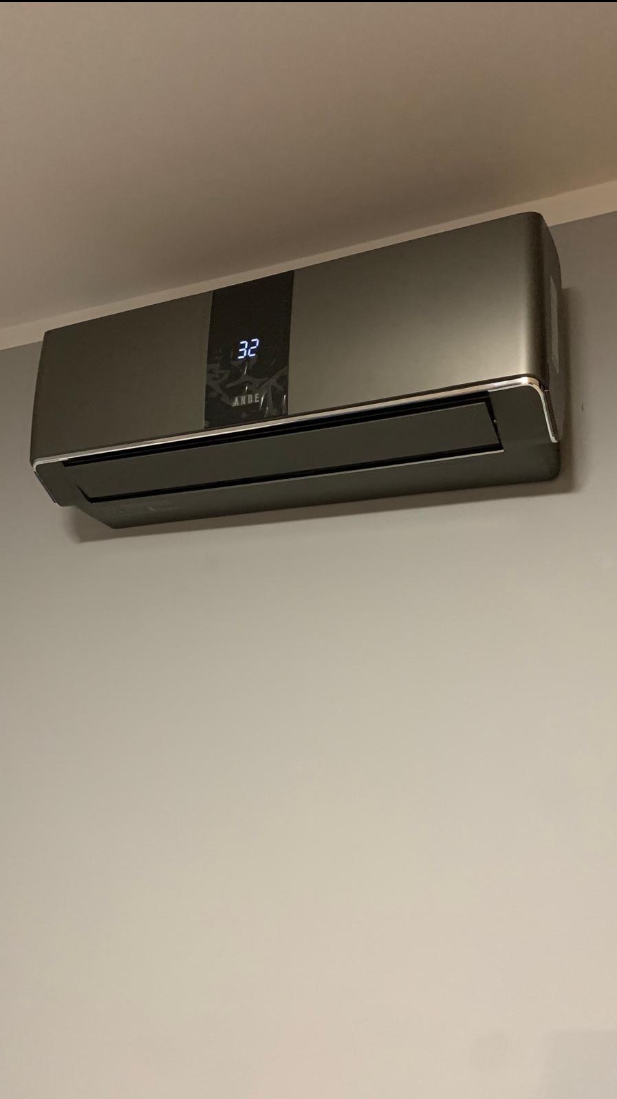 Szary klimatyzator ANDE z wyświetlaczem temperatury 32 zamontowany na ścianie. Nowoczesny design, widok z przodu, oświetlenie naturalne.