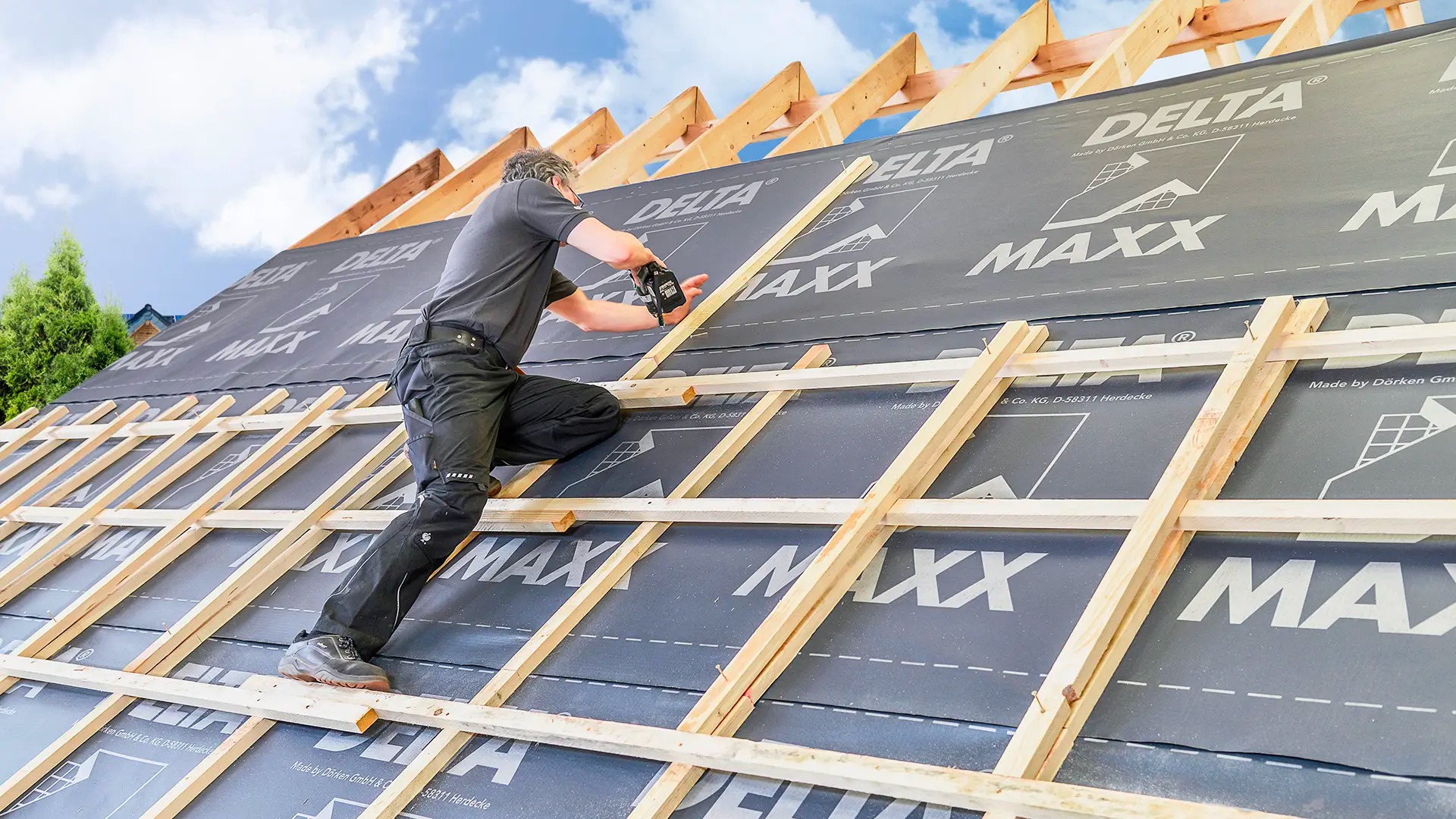 Dekarz mocuje kontrłaty na membranie dachowej Delta Maxx, widoczne fragmenty więźby dachowej i niebo