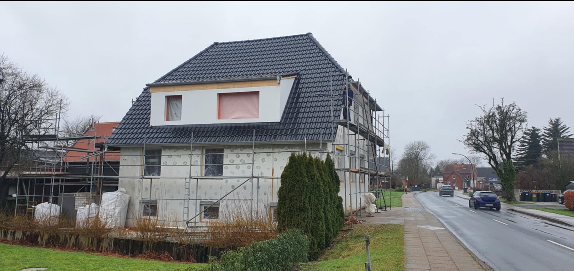 Dom w trakcie renowacji z czarnym dachem, widoczne rusztowania i zabezpieczone okna, praca w toku.