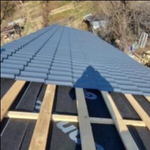 Montaż szarej blachodachówki na drewnianej konstrukcji więźby dachowej, widok z góry na fragment dachu z widoczną membraną dachową.