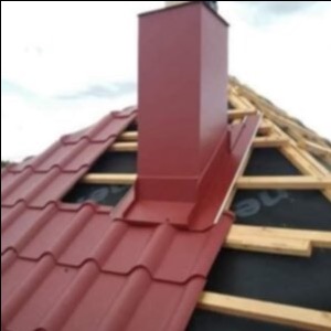 Czerwony komin z obróbką blacharską na dachu z blachodachówki, widoczna konstrukcja więźby dachowej i membrana dachowa.