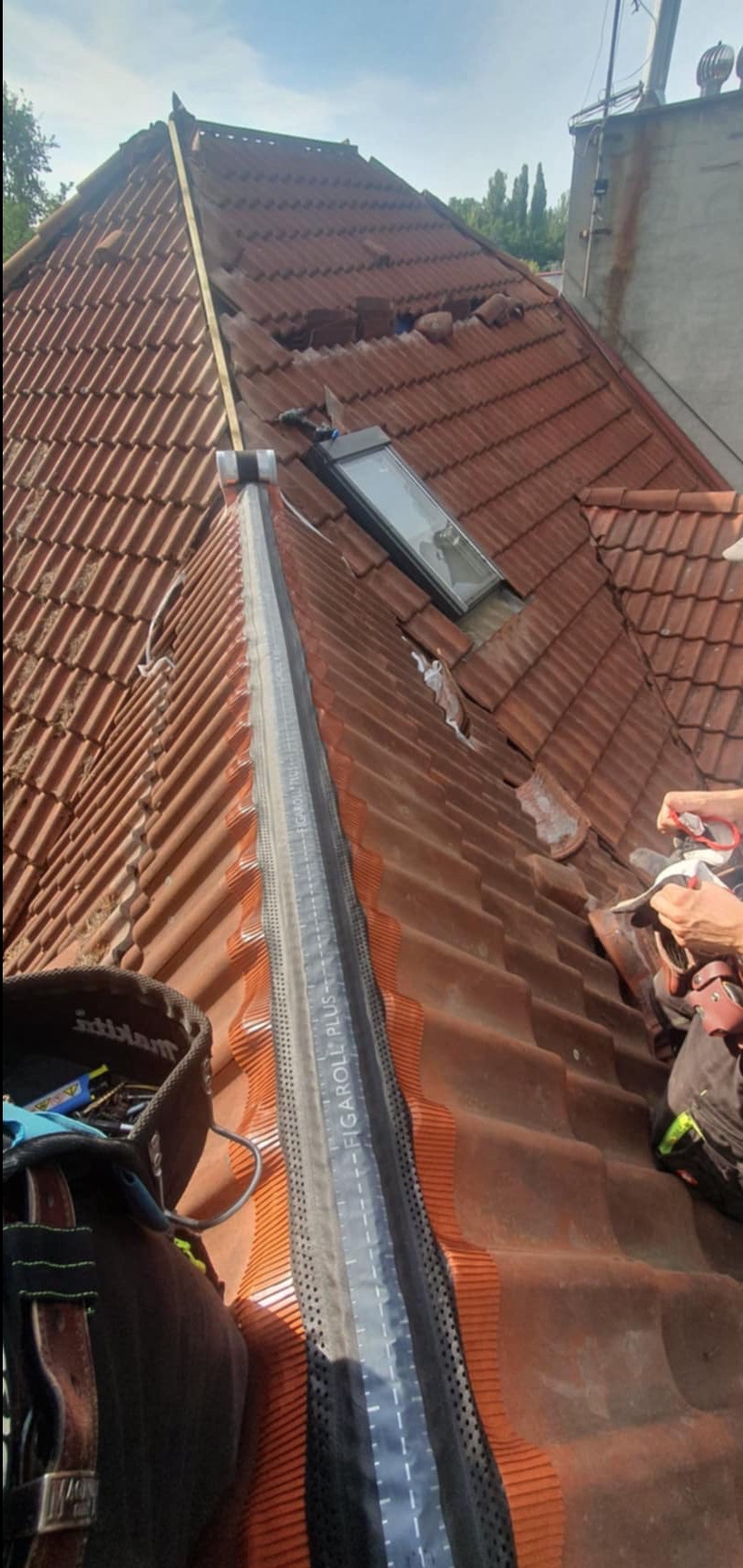 Czerwona dachówka ceramiczna z zamontowanym oknem dachowym i taśmą kalenicową Figaroll Plus, widoczne uszkodzenia w górnej części dachu