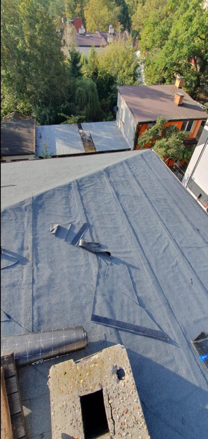 Prace dekarskie we Wrocławiu: Widok z góry na pokrycie dachu papą termozgrzewalną z widocznymi zakładkami i rolką materiału obok komina.