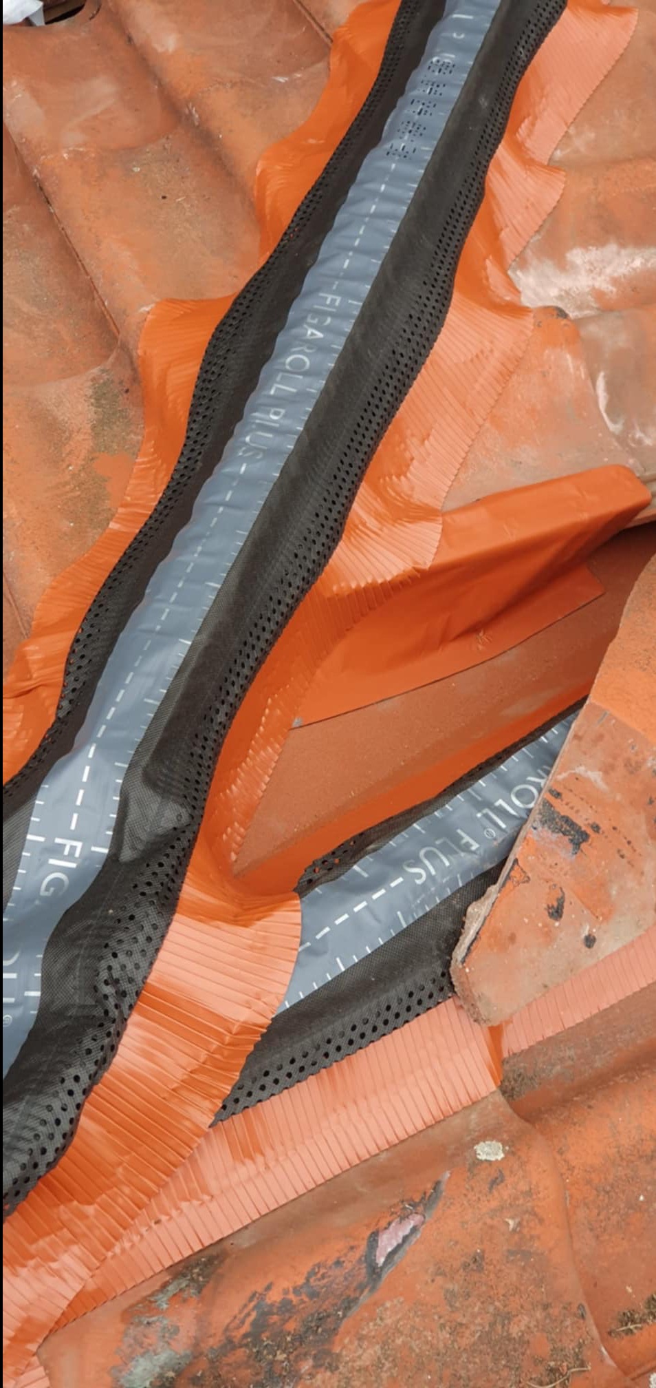 Pomarańczowe dachówki z zamontowaną membraną dachową Figaroll Plus z czarną siatką wentylacyjną, widoczne napisy na membranie.