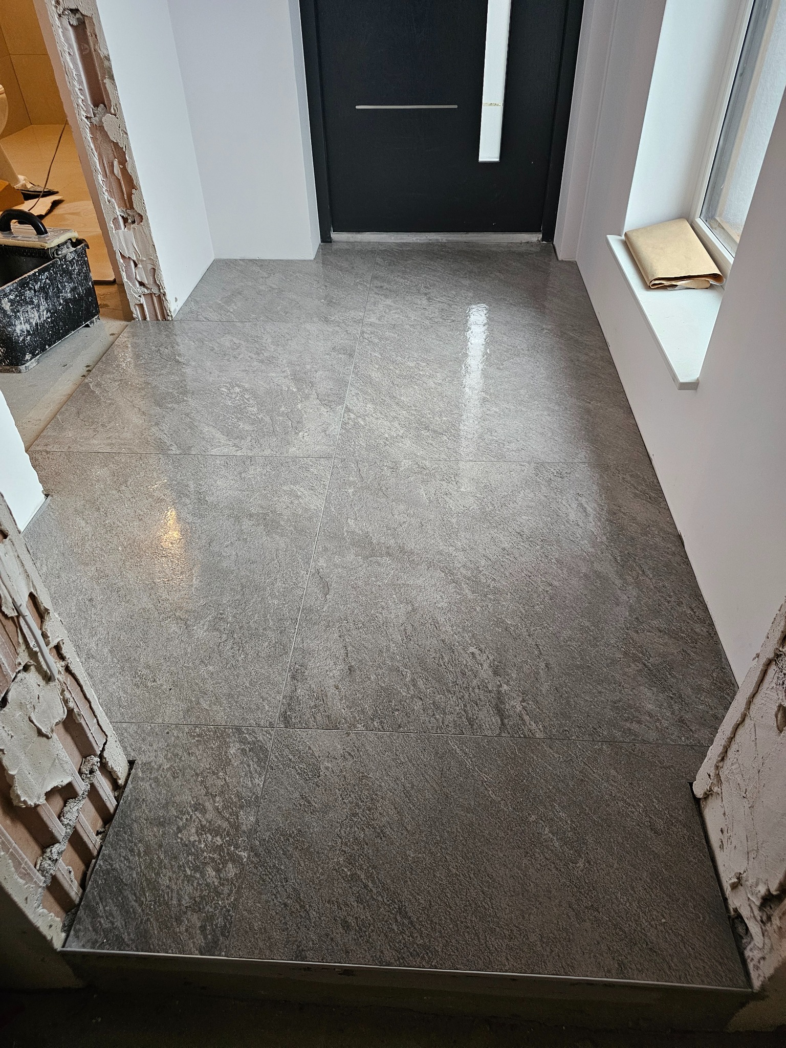 Ułożona podłoga z płytek imitujących kamień w przedpokoju, widoczne niedokończone obramowania drzwi i okna.