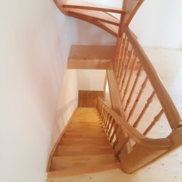 USŁUGI STOLARSKIE KOTECKI JACEK - Jasne, drewniane schody z balustradą, widziane z góry, skręcające w lewo, z widoczną podłogą z jasnego drewna i białą ścianą.