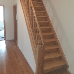 USŁUGI STOLARSKIE KOTECKI JACEK - Jasne, drewniane schody z balustradą w korytarzu z drewnianą podłogą, widoczne drzwi po lewej stronie.
