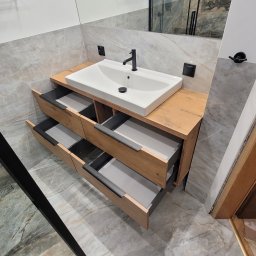 USŁUGI STOLARSKIE KOTECKI JACEK - Nowoczesna szafka łazienkowa z drewnianym blatem i umywalką nablatową; otwarte szuflady z szarymi wnętrzami; marmurowe płytki na ścianach i podłodze; widoczny fragment kabiny prysznicowej...