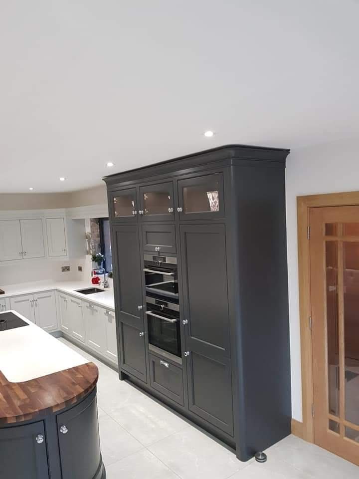 Szara zabudowa kuchenna z piekarnikami i szafkami w Bydlinie, z blatem drewnianym na wyspie kuchennej i białymi szafkami w tle.