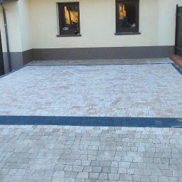 PAW-BUD Paweł Stopa - Ułożona kostka brukowa na podjeździe przed garażem, z widocznymi obrzeżami, kolumną z czerwonej cegły i narzędziami w tle.