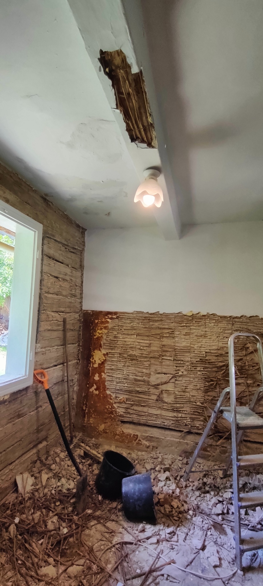 Pokój w Przeworsku w trakcie prac remontowych: odsłonięta ściana z drewnianą konstrukcją, fragment uszkodzonego sufitu, gruz na podłodze, drabina i narzędzia.