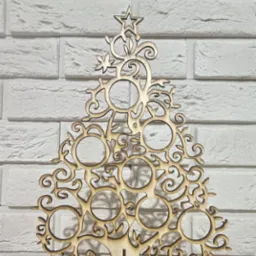 Dekoracyjna, ażurowa choinka z jasnego drewna, wycięta laserowo, na tle białej ceglanej ściany i drewnianego blatu.