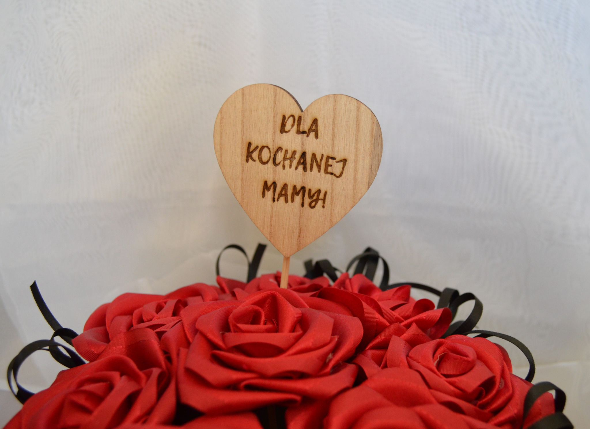 Bukiet czerwonych, satynowych róż z drewnianym sercem z napisem 'Dla Kochanej Mamy!', wykonanym techniką laserową.