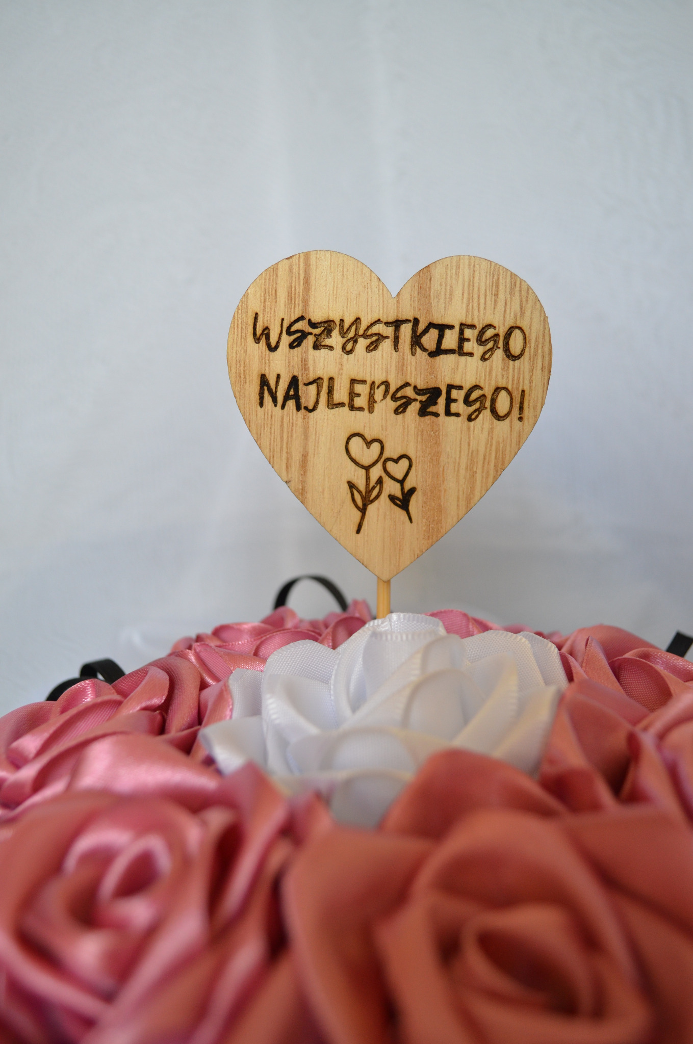 Drewniane serce z napisem 'Wszystkiego Najlepszego!' i wygrawerowanymi kwiatami, umieszczone w bukiecie różowych i białych satynowych róż.