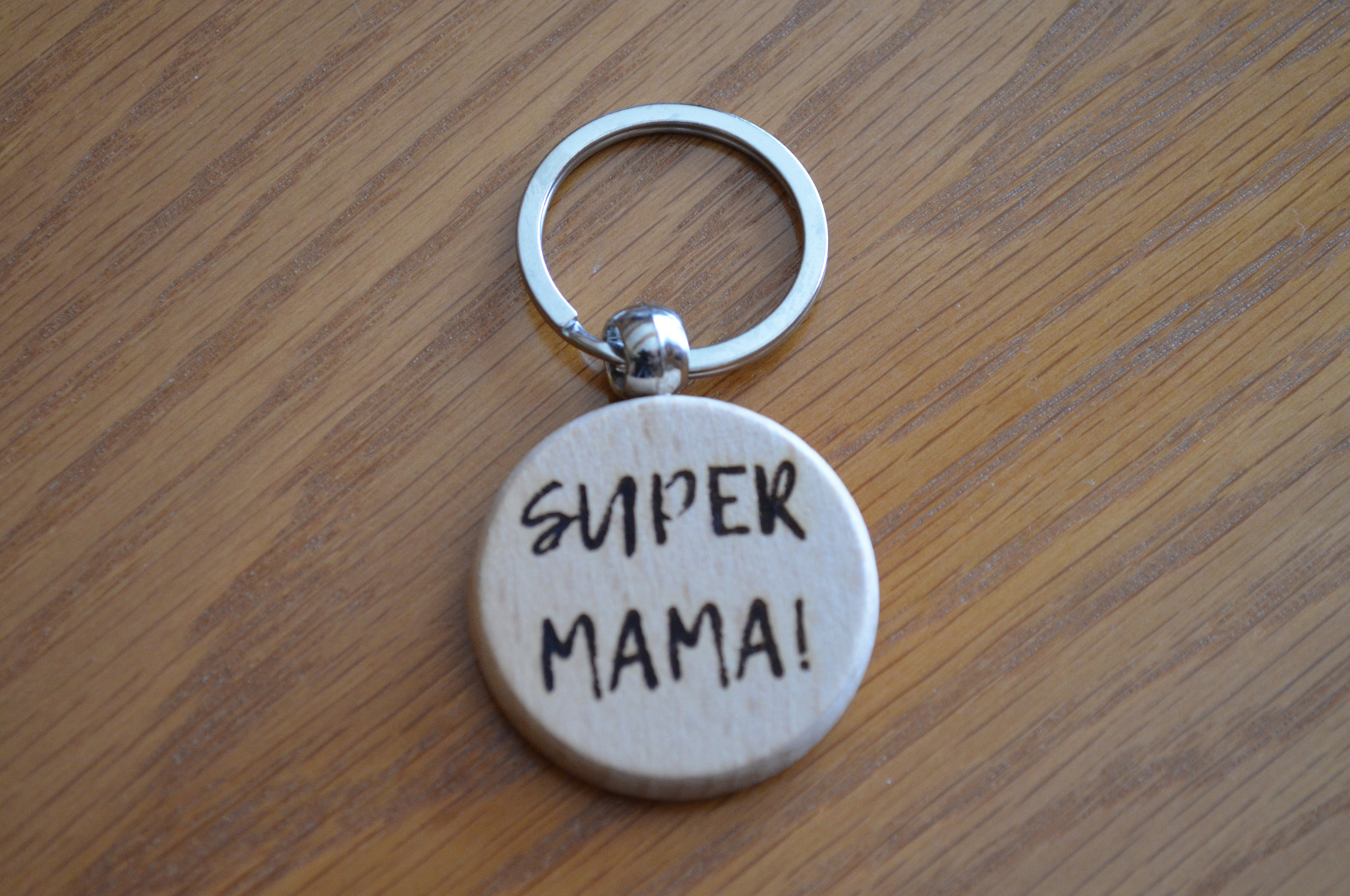Drewniany brelok z napisem 'SUPER MAMA!' leżący na drewnianym blacie.