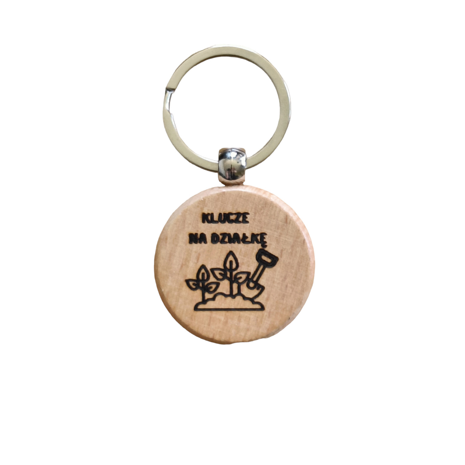Drewniany brelok z grawerem 'Klucze na działkę', przedstawiający sadzonki i łopatkę, zawieszony na metalowym kółku.