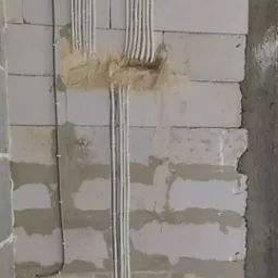 Ściana z betonu komórkowego z widocznymi przewodami elektrycznymi ułożonymi w peszlach, częściowo zamaskowanymi gipsem.